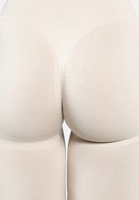 Nahaufnahme von beige-farbenen nahtlosen Leggings, die die Kontur und Textur des Stoffs an Oberschenkeln und Hüften hervorhebt.
