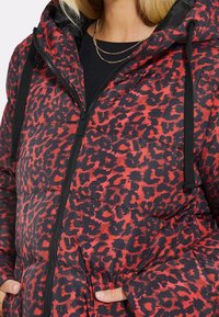 Polstret jakke i rød og sort leopardprint, med lynlåsfront, hætte med snore og to frontlommer. Glat tekstur.