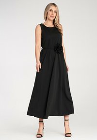 Czarna sukienka bez rękawów o płynnej linii A, z materiałowym kwiatem w talii i gładką teksturą. Elegancka, do ziemi.