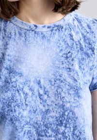 Camiseta azul de tie-dye hecha de tejido suave, con un escote redondo y mangas cortas. Variaciones de azul crean un patrón texturizado.