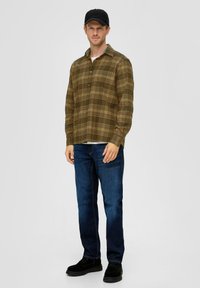 Groen en bruin geruite overhemden met lange mouwen, gecombineerd met blauwe jeans en zwarte laarzen. De persoon draagt een zwarte pet.