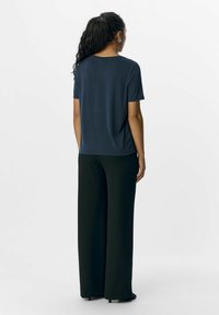 Navy blue short-sleeve t-shirt with a round neckline and loose fit, paired with black wide-leg trousers. Smooth fabric with minimal detailing.