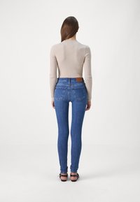 Jeans ajustados en denim azul oscuro, con dos bolsillos traseros y una etiqueta de cuero marrón. Combinados con una camiseta de manga larga de canalé beige.