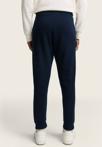 Pantalones de chándal azul marino con textura acanalada, cinturilla elástica y puños ajustados, combinados con zapatillas blancas.