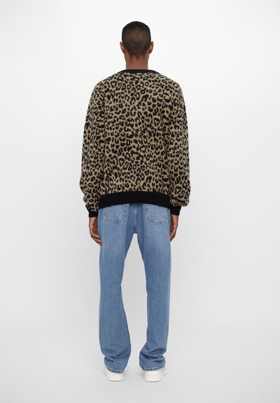 Leopard print sweater in beige and black, relaxed fit with ribbed cuffs and hem. Paired with light blue straight-leg jeans and white sneakers.