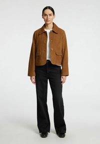 Brun ruskinds cropped jakke med spidse kraver, to frontlommer og guld-tonede knapper, parret med sorte bredbenede bukser.