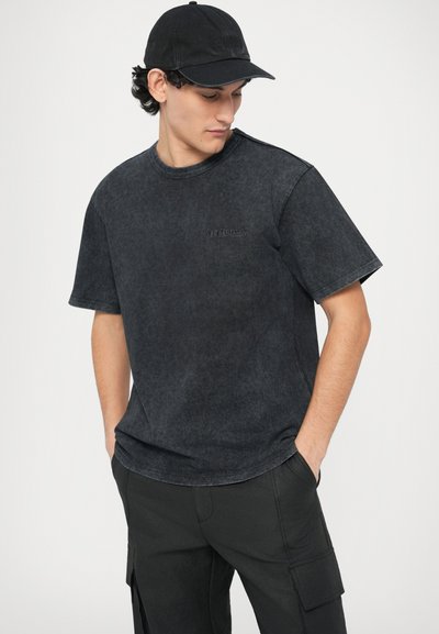 Črna majica s kratkimi rokavi z rahlo požlahtnjenim videzom in subtilnim logotipom "LES BENJAMINS". Kombinirana s črnimi cargo hlačami.