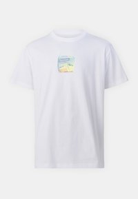 Valkoinen puuvillainen lyhythihainen t-paita, jossa on neliömäinen graafinen painatus ja sarjakuvamainen mehupurkki, jossa lukee "Cleptomania".