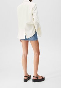 Biały żakiet o luźnym kroju, z rozcięciem z tyłu i długimi rękawami, połączony z dżinsową mini spódnicą i czarnymi sandałami na platformie.