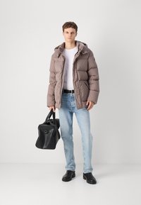 Casaco puffer castanho matelassado com capuz, t-shirt branca, jeans azul claro, bolsa preta e botas pretas chunky.