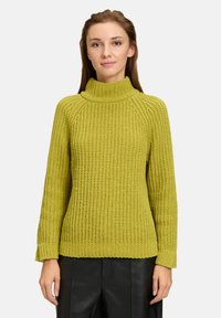Strickpulli in leuchtendem Grün mit hohem Kragen, gerippten Bündchen und strukturiertem Muster; verfügt über eine lockere Passform und lange Ärmel.