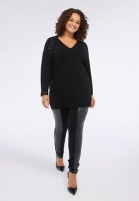 Svart tunika med v-ringning och nitar på ärmarna, kombinerad med svarta leggings i konstläder och spetsiga svarta klackar.