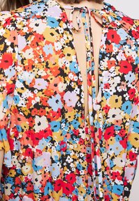 Floral blouse with a V-back design, featuring a colorful pattern of red, blue, yellow, and black on a lightweight fabric. Ties at the neck.