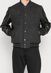Gray wool-blend varsity jacket with black leather sleeves. Features snap buttons, ribbed cuffs, and striped hem. Smooth texture overall.