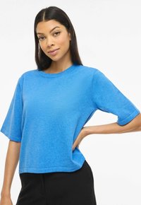 Haut bleu court à manches courtes en tissu doux, avec un col rond et des revers roulés, assorti à un pantalon noir.