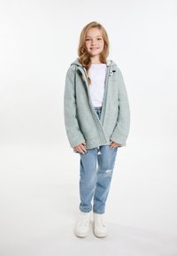 Ljusgrå zip-up huvtröja med ett mjukt innerfoder, tillsammans med ljusblå slitna jeans och vita högskaftade sneakers.
