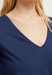 Námořnická modrá V-krková trička vyrobené z měkké bavlněné tkaniny, s hladkým povrchem a čistým švem kolem výstřihu a ramen.