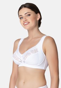 Biały biustonosz z kwiatowym koronkowym zdobieniem, szerokimi ramiączkami i falistymi krawędziami. Miękki materiał o gładkiej fakturze oraz delikatną kokardką na środku.