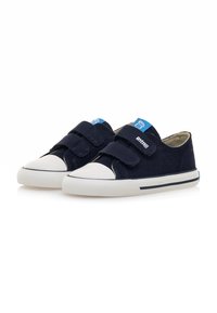 Zapatos de tela color marino con punta y suela de goma blanca, que cuentan con dos correas de velcro y un logo azul en la lengüeta.