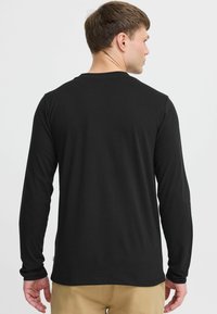 Zwarte longsleeve shirt van zacht materiaal, met een ronde hals en aansluitende mouwen. Glad textuur zonder zichtbare patronen of accenten.
