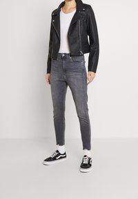 Chaqueta de motorista negra de cuero con herrajes plateados, jeans grises de tiro alto con dobladillos deshilachados y zapatillas negras con detalles y cordones blancos.