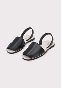 Sandalias slingback de cuero negro con punta abierta, con un acabado suave, detalles cosidos y una plantilla y suela de color beige.
