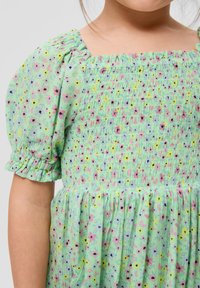 Grünes Blumenkleid aus strukturiertem Stoff mit Puffärmeln, das rosa, gelbe und schwarze Blumen in einem gerafften Design zeigt.