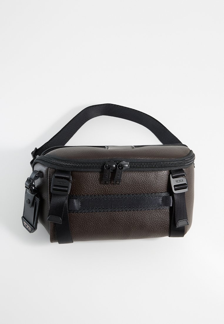 Braune strukturierte Tasche mit einem schwarzen Reißverschluss, verstellbarem Tragegurt und vorderem Netzfach, ausgestattet mit stabilen Clips und einem flachen Boden für Stabilität.