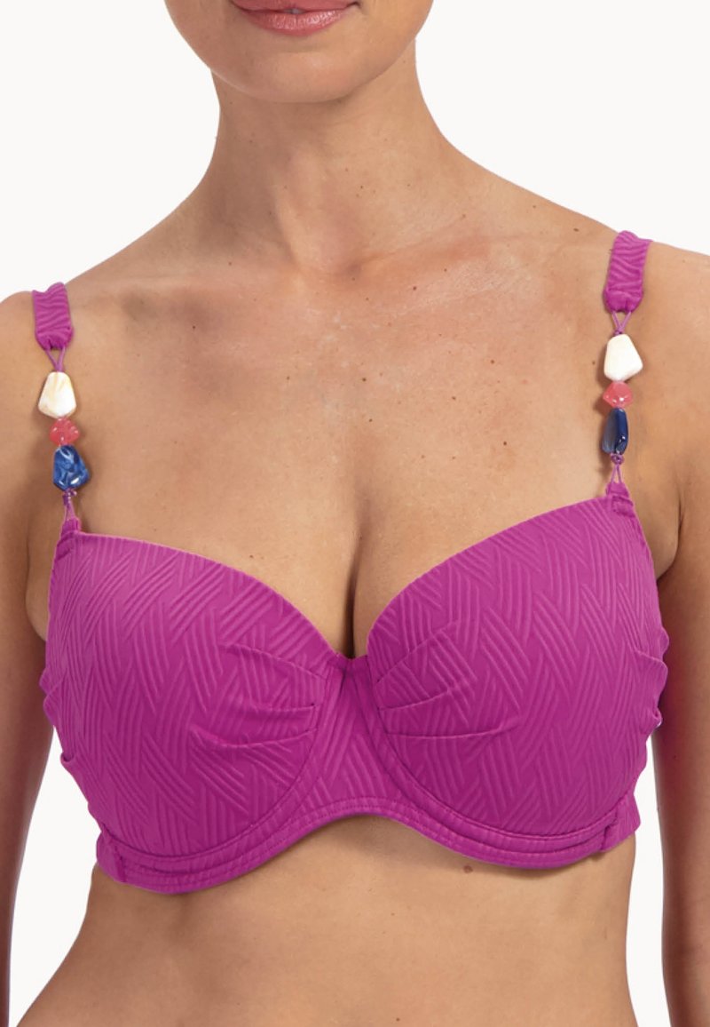 Kobieta w teksturowanym fioletowym biustonoszu z formowanymi miseczkami i ozdobnymi koralikami na regulowanych ramiączkach na białym tle.