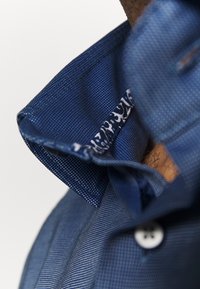 Gros plan d'un col de chemise texturée bleue avec un petit détail en tissu à motifs à l'intérieur du col.