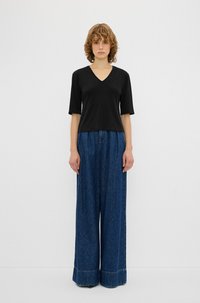 Sort v-hals t-shirt med korte ærmer, parret med brede blå denimbukser med en subtil søm. Glat tekstur hele vejen igennem.