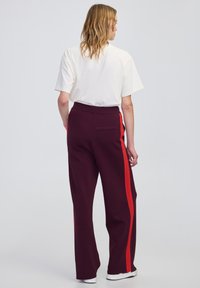 Bordowe spodnie typu wide-leg z czerwonymi paskami po bokach, prążkowana tekstura, elastyczny pas i tylna kieszeń, połączone z gładką białą koszulką.