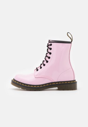Skinnende pink læder snørebåren kampstøvle med sort sål med gul syning og en sort trækflig bagpå.