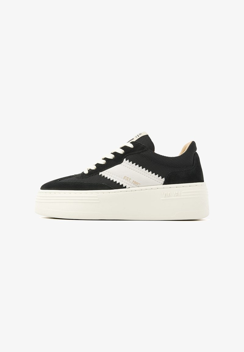 Black sneaker with white accents, textured fabric upper, round toe, and a thick white platform sole. Features prominent zigzag pattern on the side.
