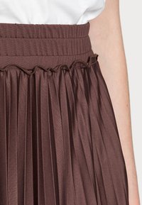 Jupe plissée marron avec une taille élastique côtelée. Présente un détail froncé le long de la taille, mettant en valeur un tissu texturé.