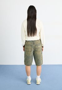 Pantalones cortos de mezclilla en azul desgastado con un corte relajado; cuentan con bolsillos traseros y un dobladillo deshilachado. Se llevan con una camisa de manga larga de color claro y zapatillas.