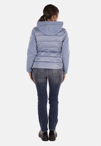 Giacca a vento leggera blu chiaro con cappuccio, design trapuntato e polsini elasticizzati, abbinata a jeans in denim scuro e scarpe con zeppa nere.