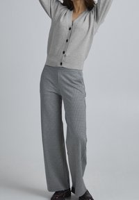 Ljusgrå stickad cardigan med V-ringning och mörka knappar, kombinerad med höga svarta och vita houndstooth byxor med vida ben.