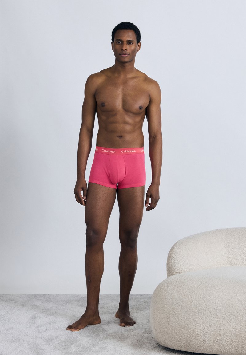Calzoncillos bóxer de algodón rojo con cintura elástica Calvin Klein, modelados en una figura masculina de piel desnuda en un ambiente neutral.