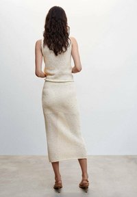 Ensemble deux pièces en maille comprenant un haut sans manches et une jupe mi-longue de couleur beige clair, avec un motif texturé à mailles ajourées.