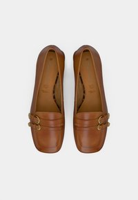 Καφέ δερμάτινα παπούτσια flats με στρογγυλή μύτη, που διαθέτουν δύο χρυσές πόρπες και λεία υφή. Ανοιχτές πλευρές και μινιμαλιστικός σχεδιασμός.