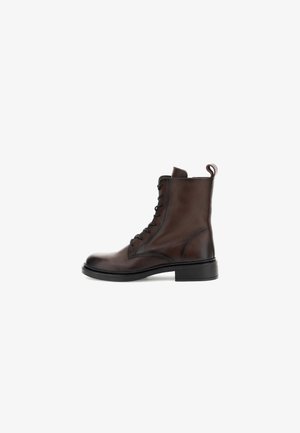 Bottines en cuir marron avec un laçage, texture lisse, bout rond et semelle en caoutchouc noir robuste. Possède une languette à l'arrière.