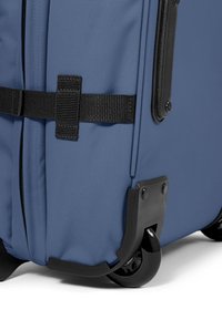 Blue fabric suitcase with a textured exterior, black straps, and two wheels, featuring a hard plastic base for durability.