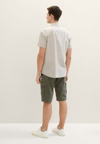 Camisa de manga corta en gris claro con botones y pantalones cortos de cargo en verde oliva. Zapatillas blancas. Bolsillos visibles en los pantalones cortos. Diseño simple y casual.
