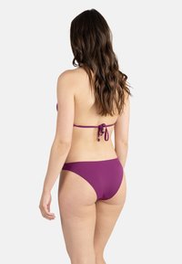 Ensemble bikini violet avec fermeture à nouer dans le dos. Le haut a des bretelles fines et le bas est taille basse avec une texture lisse et une couverture minimale.