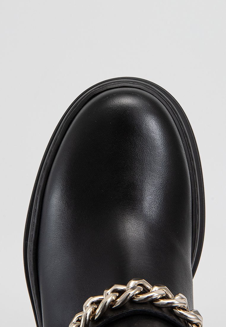 Schwarze Lederstiefel mit abgerundetem Zeh, robuster Bauweise und einem auffälligen silbernen Kettenakzent an der Vorderseite. Glatte Textur.