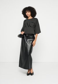 Krátké tmavě šedé tričko s velkým černým potiskem, kombinované s dlouhou černou koženou sukní a odpovídajícími černými botami na podpatku. Součástí je černá taška.