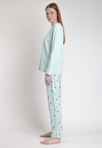 Conjunto de pijama verde menta que incluye una camiseta de manga larga y pantalones con estampado de pingüinos. Tejido suave con un ajuste holgado y escote redondo.