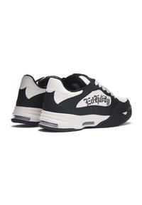 Scarpe atletiche in bianco e nero con tomaia in pelle strutturata, colletto imbottito e ammortizzazione traslucida. Logo del marchio visibile in modo prominente.