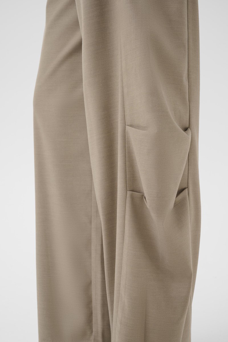 Beige pants with a loose fit featuring a large, rectangular side pocket with folds and seams visible on the fabric.